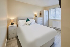 A modern bedroom with a large bed, bedside tables, a dresser, and a window with blinds.