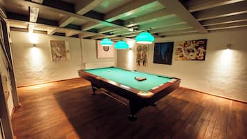 Una mesa de billar en una habitación con suelo de madera y vigas a la vista.