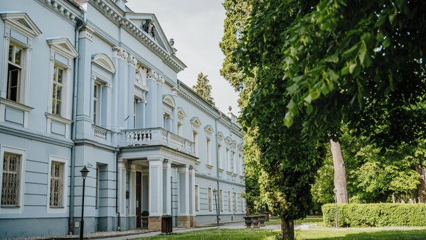 A large, light blue building with classical architecture, including columns and decorative moldings.