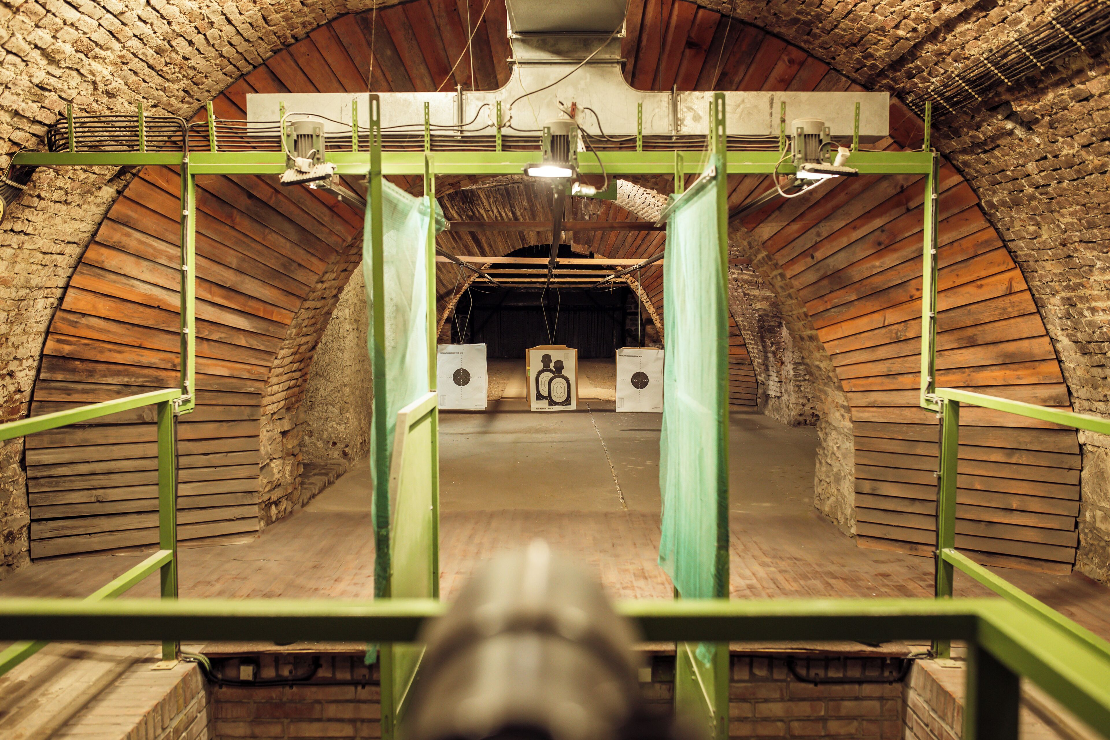 Een tunnel met bakstenen muren, een gewelfde boog, een groene metalen hekwerk en een centraal lichtarmatuur.