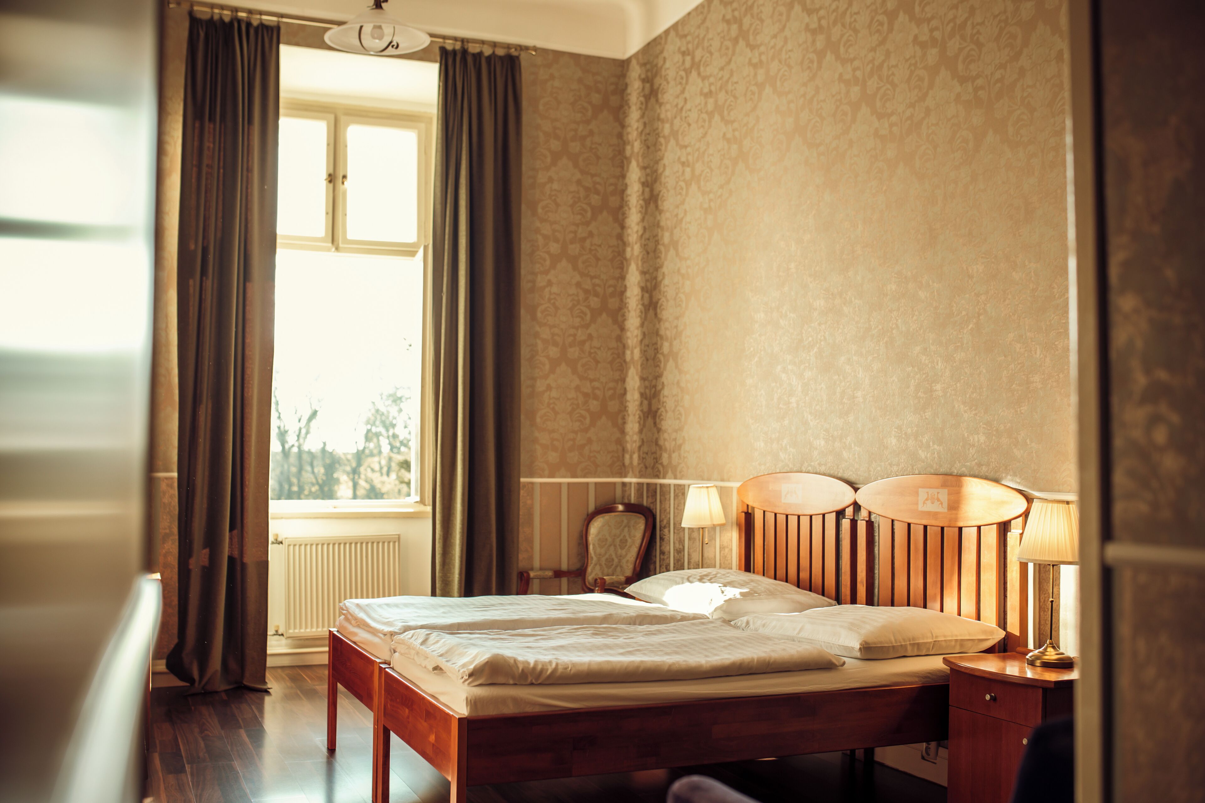 A hotel room with a wooden bed, two bedside lamps, a chair, and a window with curtains.