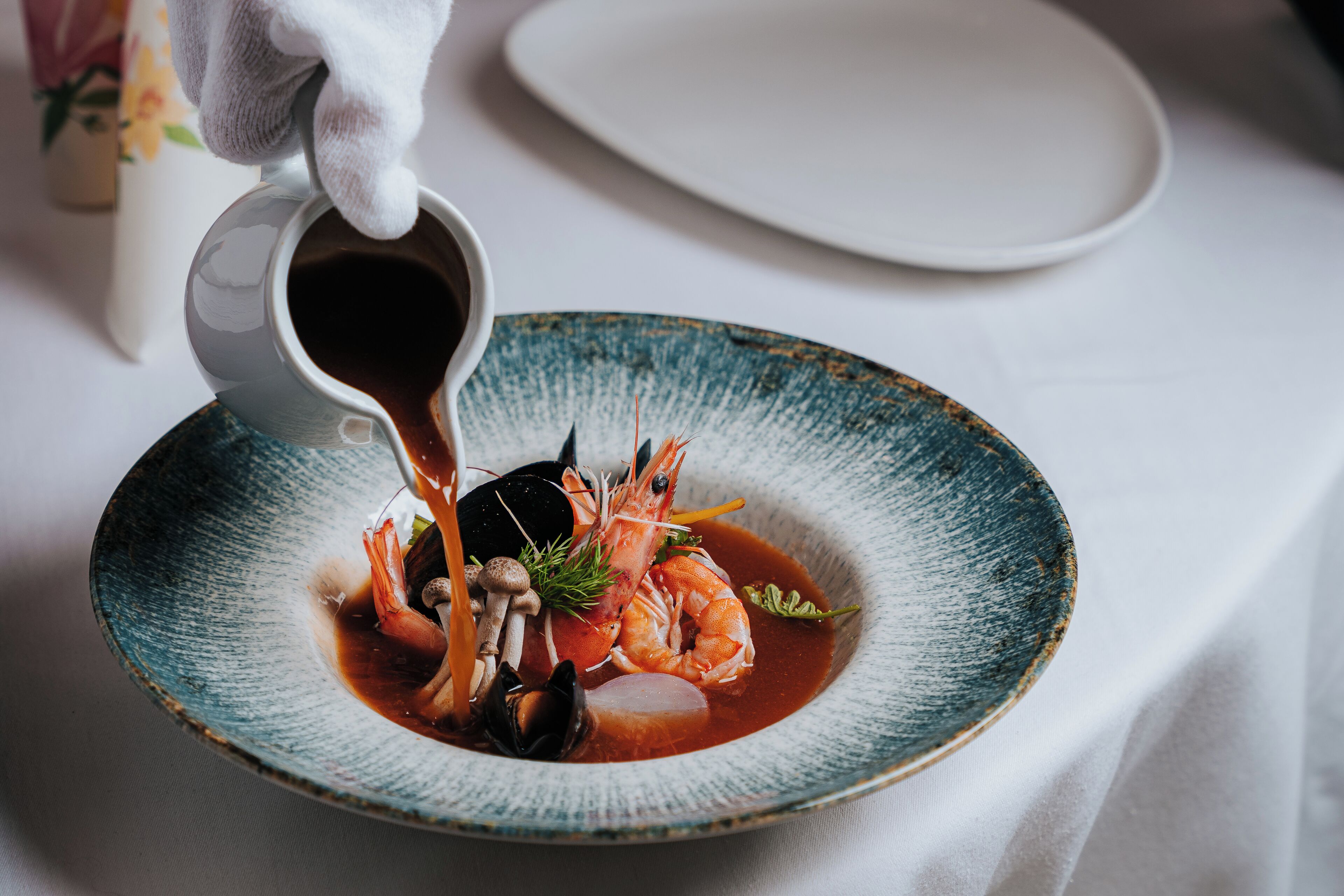 Un plato de mariscos con camarones y mejillones en un taz ón azul, siendo bañado con salsa.