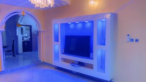 Una sala de estar moderna con un televisor de pantalla plana grande montado en una pared blanca, iluminación ambiental y un candelabro.