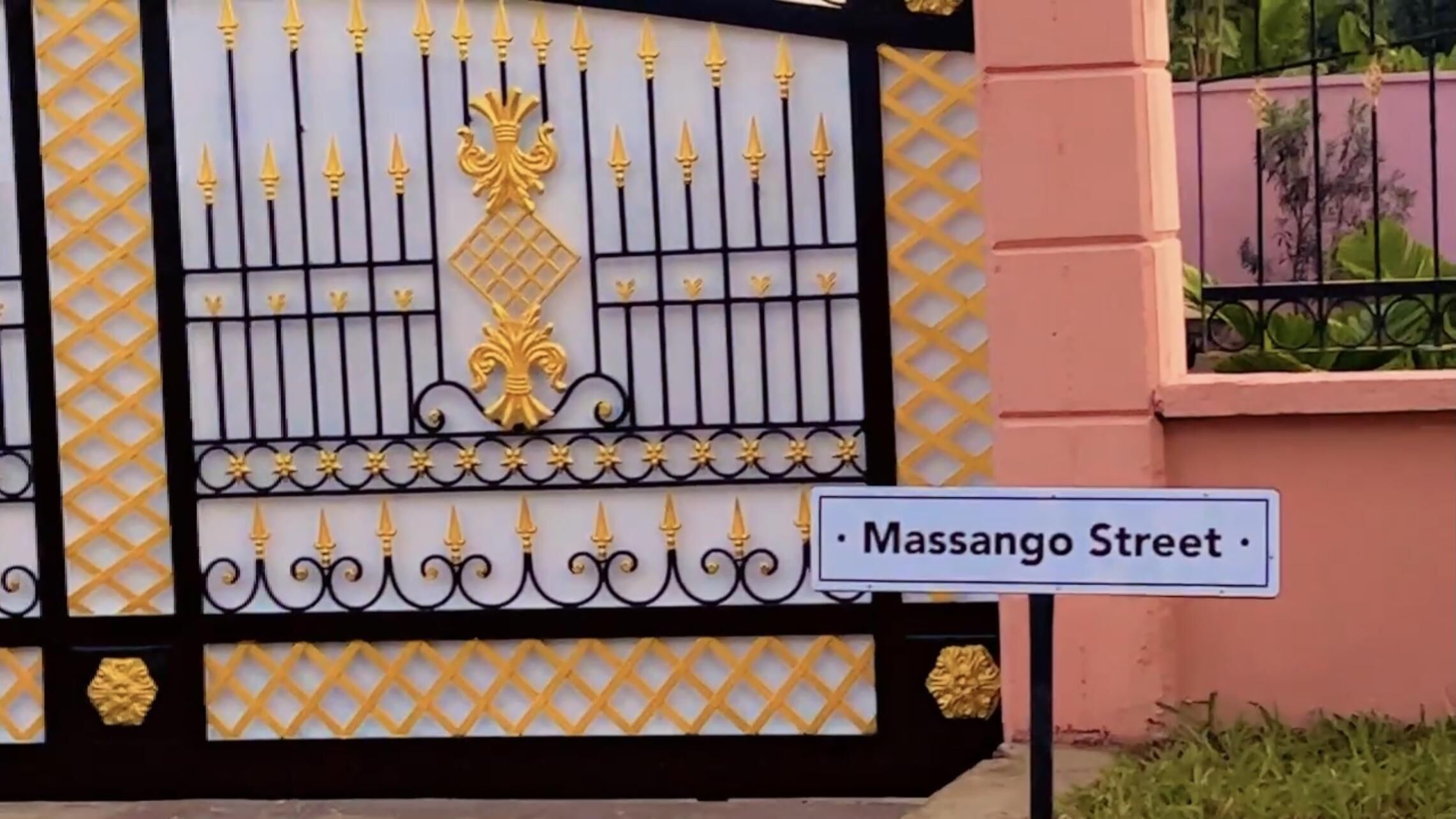 Une entrée fermée par un portail orné de motifs en métal et un panneau de rue indiquant « rue Massango ».