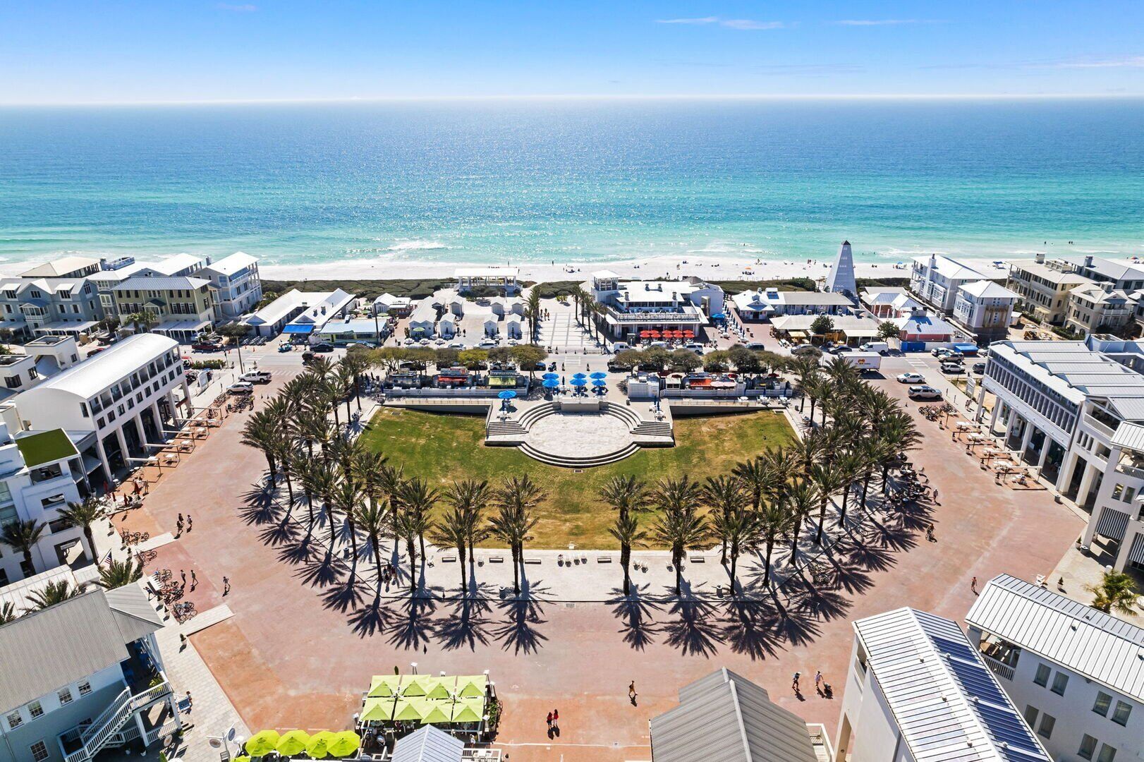 A coastal urban area with a central plaza surrounded by buildings, a beach, and palm trees.