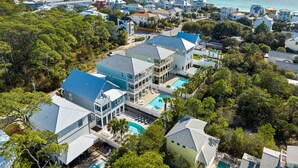 A coastal residential area with modern houses, a large swimming pool, and a view of the ocean. - Seagrove - 1 Block from Beach, Golf Cart, Private HEATED Pool, Game Room, Bikes & Tesla Charger! (Santa Rosa Beach)