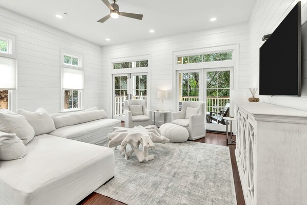A spacious living room with a white sofa, two armchairs, a round coffee table, and a fireplace. Large windows provide natural light and views of the outdoors. - WaterColor Beach Club, Bikes, 3 Min Walk to Seaside (Santa Rosa Beach)