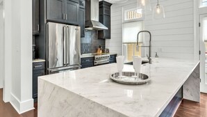 A modern kitchen with dark cabinetry, stainless steel appliances, and a marble island.