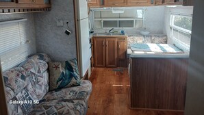 Een compacte RV-keuken met houten kastjes, een koelkast, een wastafel en een klein zitehoekje.