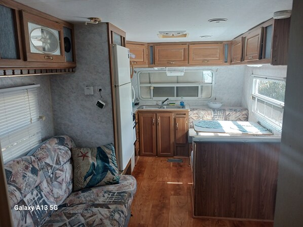 Une cuisine compacte pour camping-car, avec des placards en bois, un réfrigérateur, un évier et un petit coin repas.