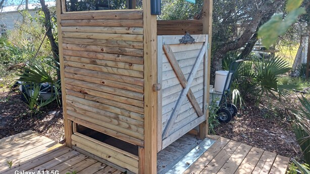 Een houten constructie met een schuin dak en een raam, omgeven door groen.