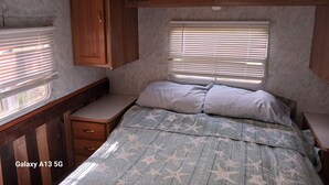Een compact interieur van een camper, met een bed, een zithoekje en houten kasten.
