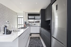 A modern kitchen with a large stainless steel refrigerator, white cabinetry, and a black and white patterned rug. - Blouberg Heights 406 (Cape Town)