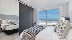 A modern hotel room with a large bed, a view of the ocean, and a sliding door. - Blouberg Heights 406 (Cape Town)