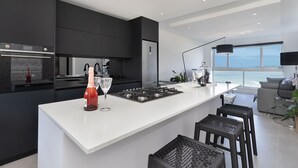 A modern kitchen with a central island, black cabinets, and a view of the ocean. - Blouberg Heights 406 (Cape Town)