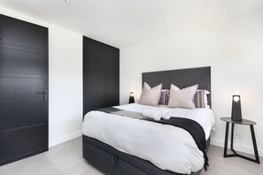 A modern bedroom with a large bed, dark wood wardrobe, and bedside lamps. - Blouberg Heights 406 (Cape Town)