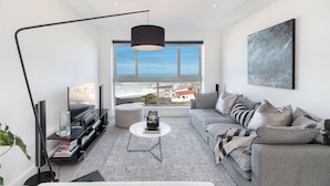 A modern living room with a large window, a sofa, a coffee table, and a TV on a stand. - Blouberg Heights 406 (Cape Town)