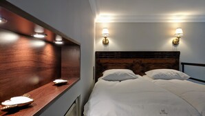 Une chambre d’hôtel avec une tête de lit en bois, deux lampes de chevet et une table de chevet avec une lampe et une horloge.