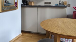 Une cuisine moderne avec des meubles blancs, une table à manger en bois et un grand miroir.