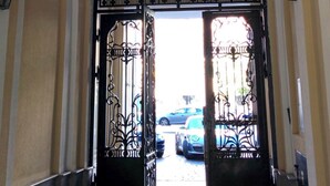 Un couloir mène à une entrée fermée par un portail en métal et illuminée par un luminaire suspendu.