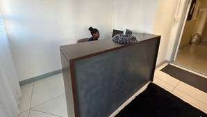 A reception desk with a person seated behind it, a black rug in front, and a tiled floor. - 57onWYNNE (Cape Town)