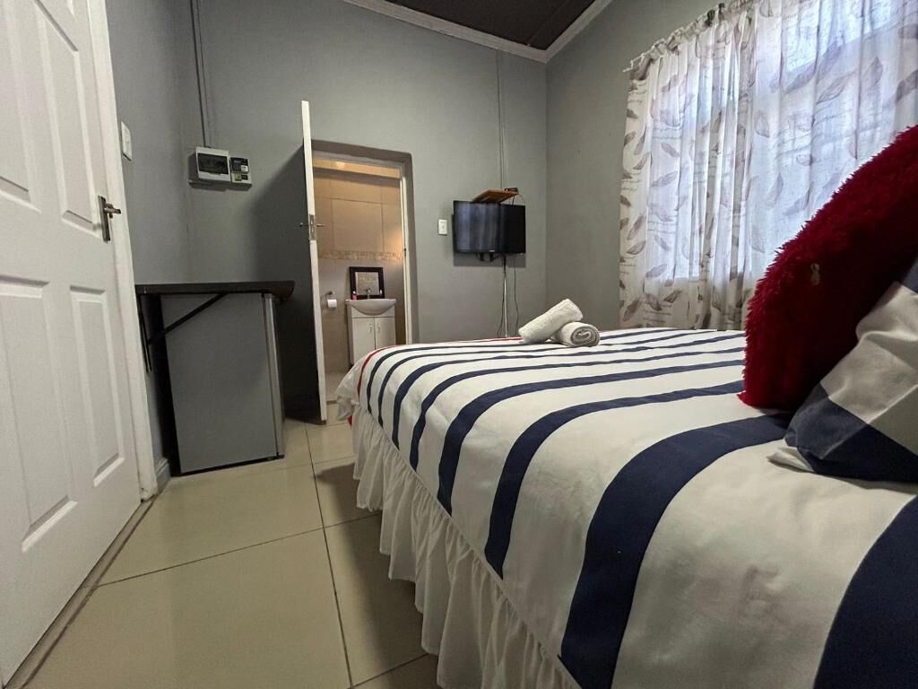 A bedroom with a bed, a TV, a small desk, and a bathroom door.