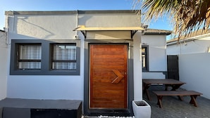 A small building with a wooden door, two windows, and a bench outside. - 57onWYNNE (Cape Town)