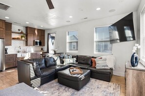 A modern living room with a sectional sofa, a coffee table, and a kitchen area with wooden cabinets and a microwave.