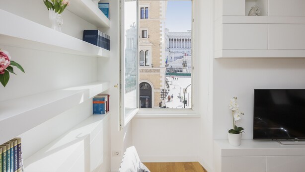 A modern living room with a large window, a flat-screen TV, and a bookshelf.