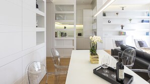 A modern kitchen with white cabinetry, a dining area with a white table, and a living area with a sofa and chairs.