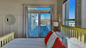 Ein Schlafzimmer mit einem großen Bett, Blick auf den Strand und einem Balkon mit Geländer.