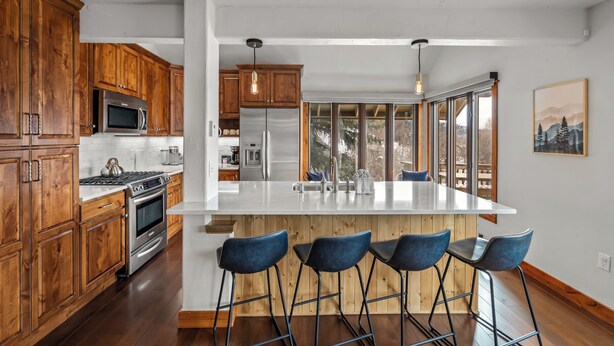 Una cocina moderna con armarios de madera, electrodomésticos de acero inoxidable, una isla grande con taburetes de bar y ventanas amplias con vistas al exterior.
