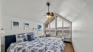 Un dormitorio con cama, ventilador de techo, ventana con persianas y decoración en las paredes.
