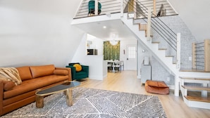 Un loft moderne avec de hauts plafonds, un escalier aux poutres apparentes et un espace de vie chaleureux comprenant un canapé et une table basse.