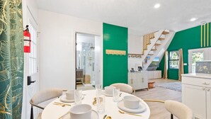 Un espace repas avec une table ronde dressée pour six personnes, un escalier et un coin cuisine.