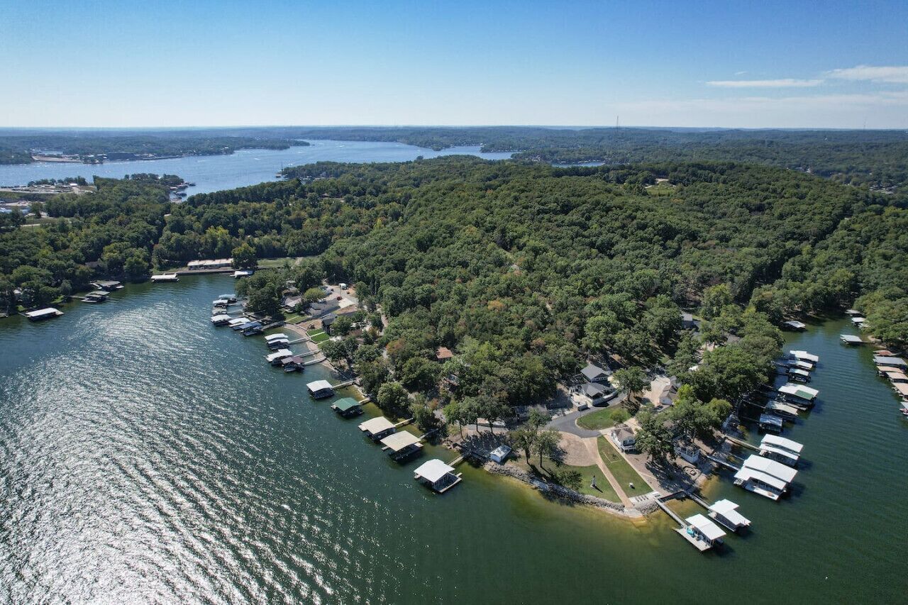 An aerial view of a lakeside property with several docked boats, surrounded by dense forest.