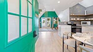 Une cuisine moderne avec un coin repas, agrémentée d’un mur d’accent vert, de meubles blancs et d’un escalier en bois.
