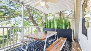 A covered outdoor patio with a table and benches, surrounded by greenery and trees.