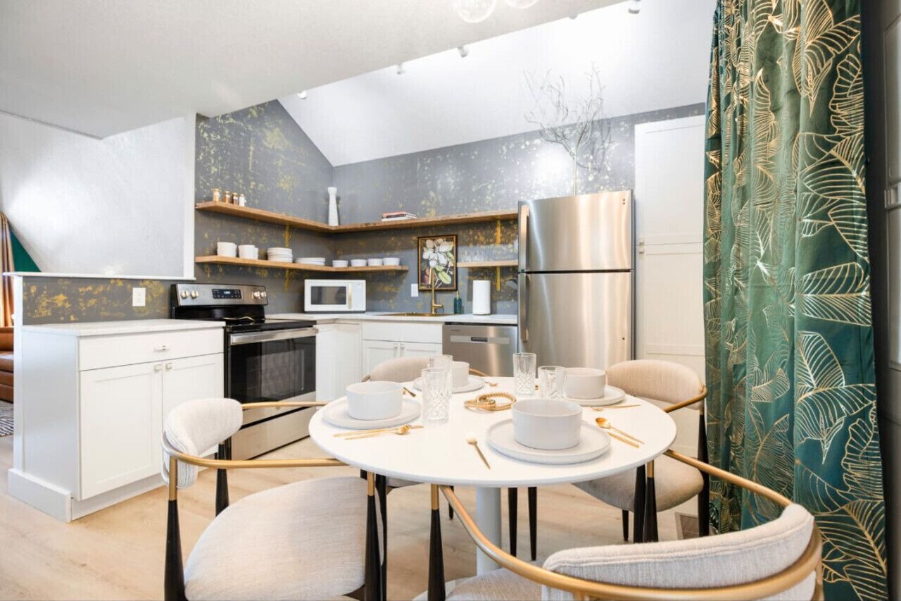 A modern kitchen with white cabinetry, a stainless steel refrigerator, and a dining area with a round table and chairs.