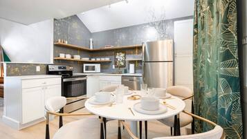 A modern kitchen with white cabinetry, a stainless steel refrigerator, and a dining area with a round table and chairs.