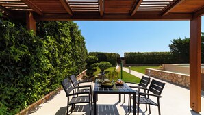 An outdoor patio with a table and chairs, surrounded by greenery and a clear sky.