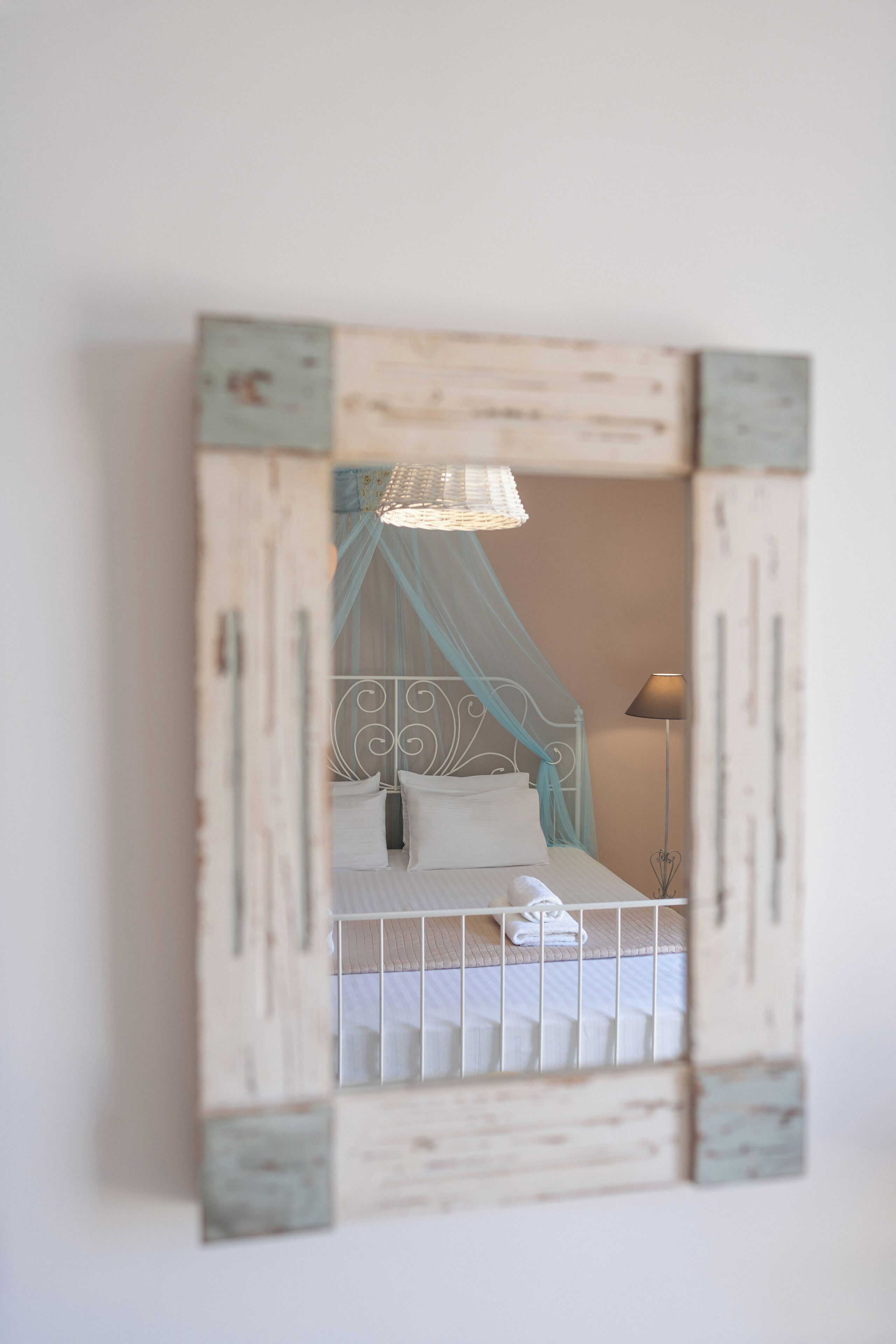 A bed with a canopy, a bedside lamp, and a wall-mounted mirror with a rustic frame.