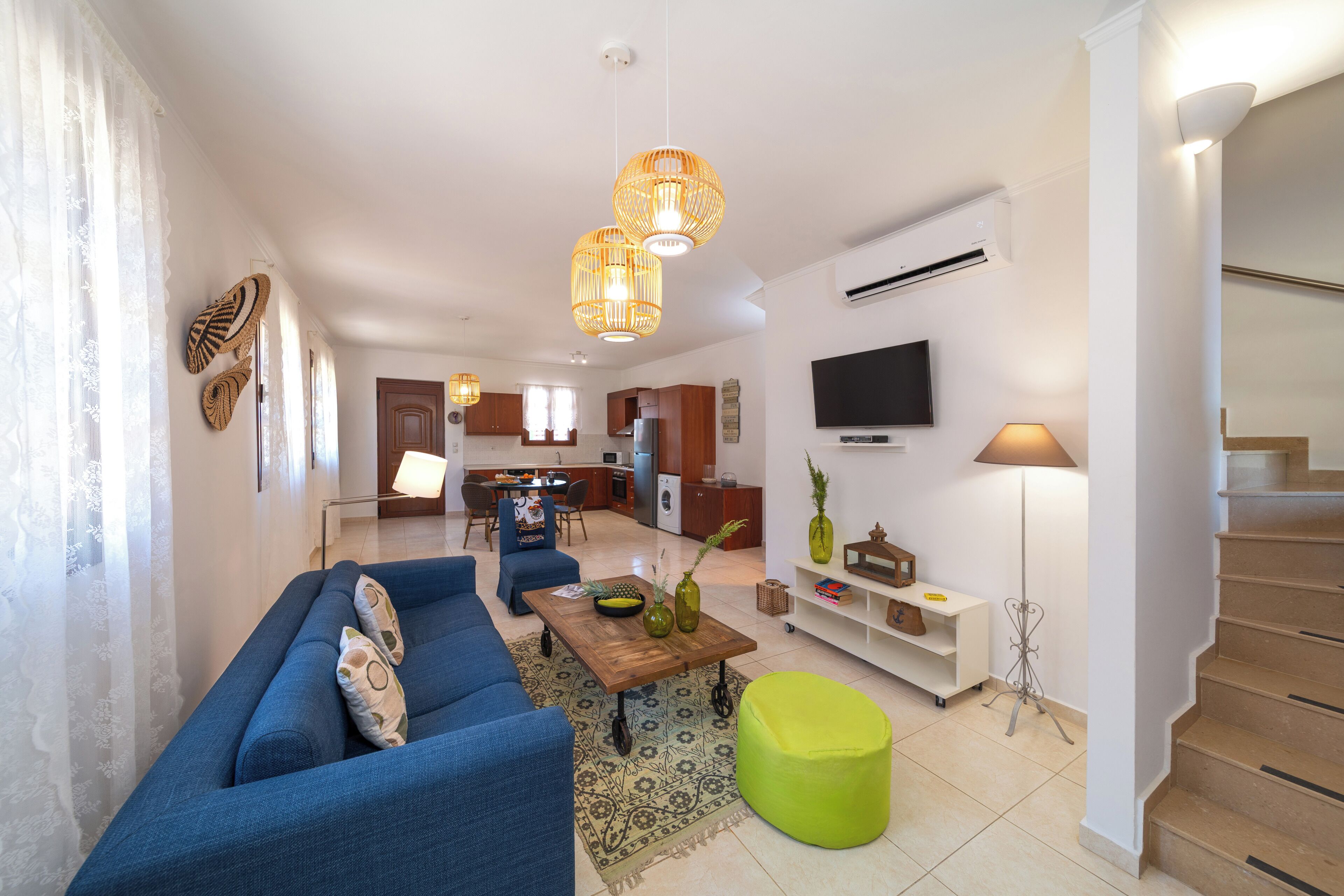 A modern living room with a blue sofa, a green ottoman, and a kitchen in the background.