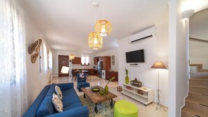 A modern living room with a blue sofa, a green ottoman, and a kitchen in the background.
