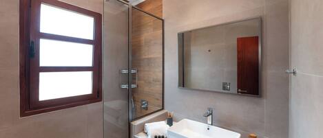 A modern bathroom with a glass shower enclosure, a large mirror, and a marble countertop.
