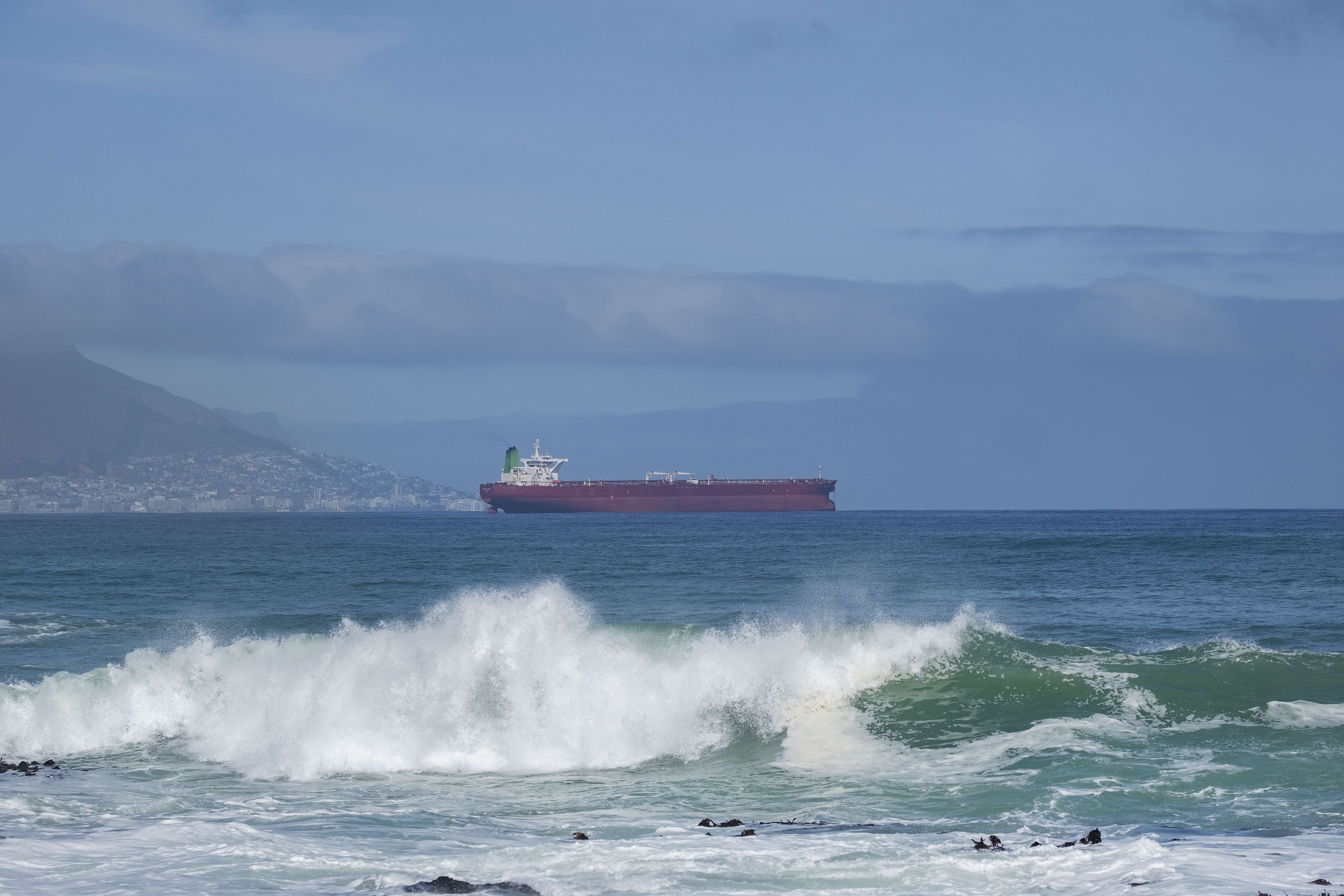 A large cargo ship on the ocean with waves crashing onto the shore.