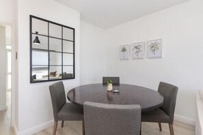 A round dining table with four grey upholstered chairs, a black-framed mirror, and three framed palm tree pictures on the wall. - Blouberg Heights 207 (Cape Town)