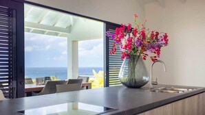 A modern kitchen with a large window, a vase of flowers, and a view of the ocean. - Modern Vibrant Villa with Terrace & Private Pool (Curacao)