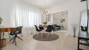 Un salon moderne avec un coin repas, comprenant une table ronde, des chaises noires et un canapé gris.