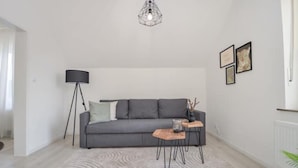 Un salon moderne avec un canapé gris, une petite table d’appoint en bois, un lampadaire et un tapis à motifs.